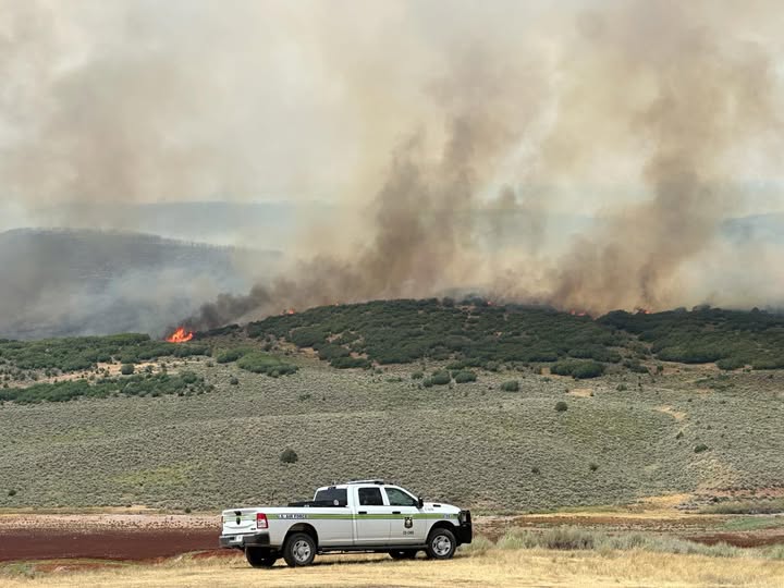Lee Fire afternoon update image of smoke and open flame on a ridge with a fire personnel truck nearby
